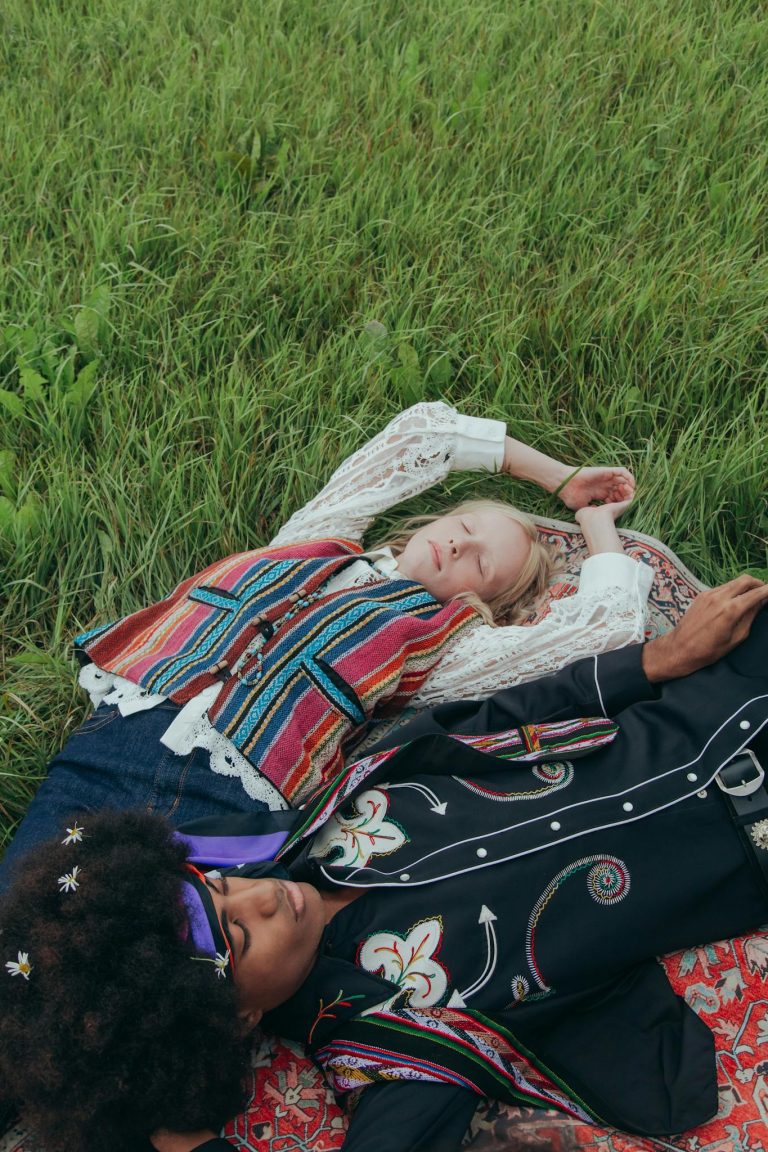 A couple in vibrant clothing relaxes on grass, showcasing a blend of cultures and harmony.