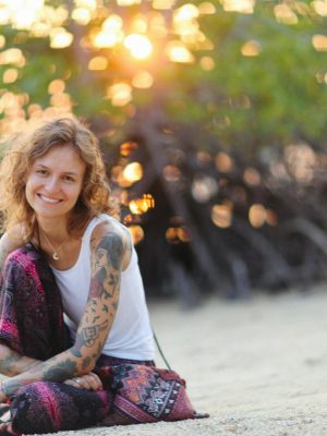 Caucasian woman with tattoos sitting on a sandy beach, enjoying the sunset.